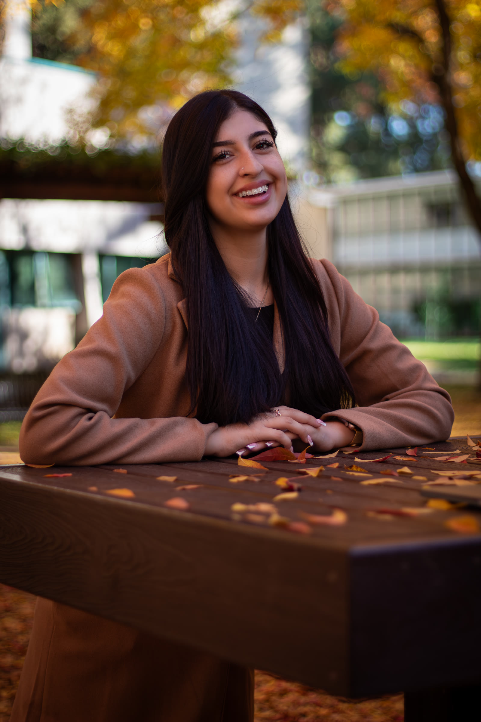 Woman smiling at a wooden table scattered with autumn leaves