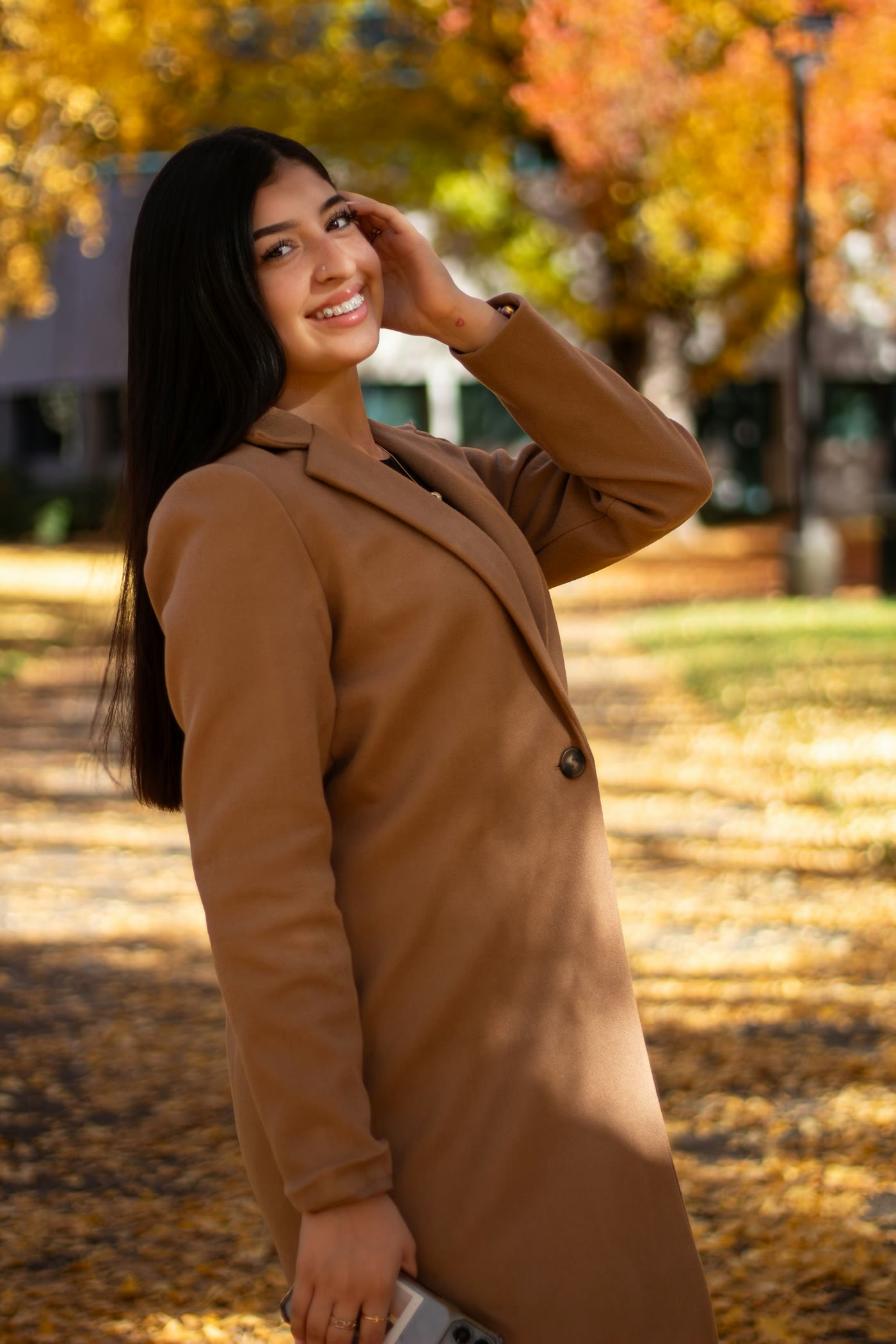 Woman in a brown coat beneath autumn trees