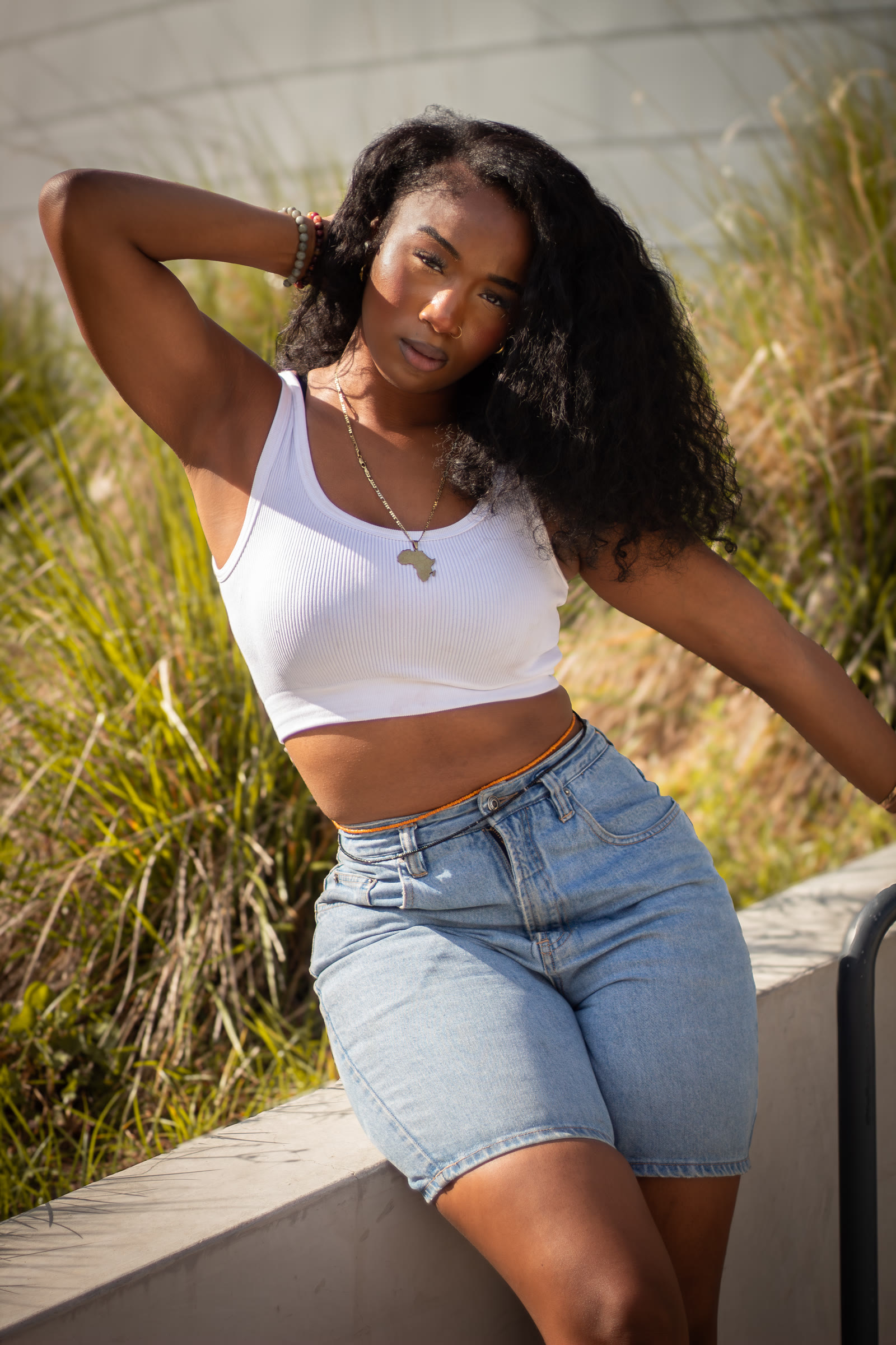 Sunlit portrait of a woman in a white top beside ornamental grasses